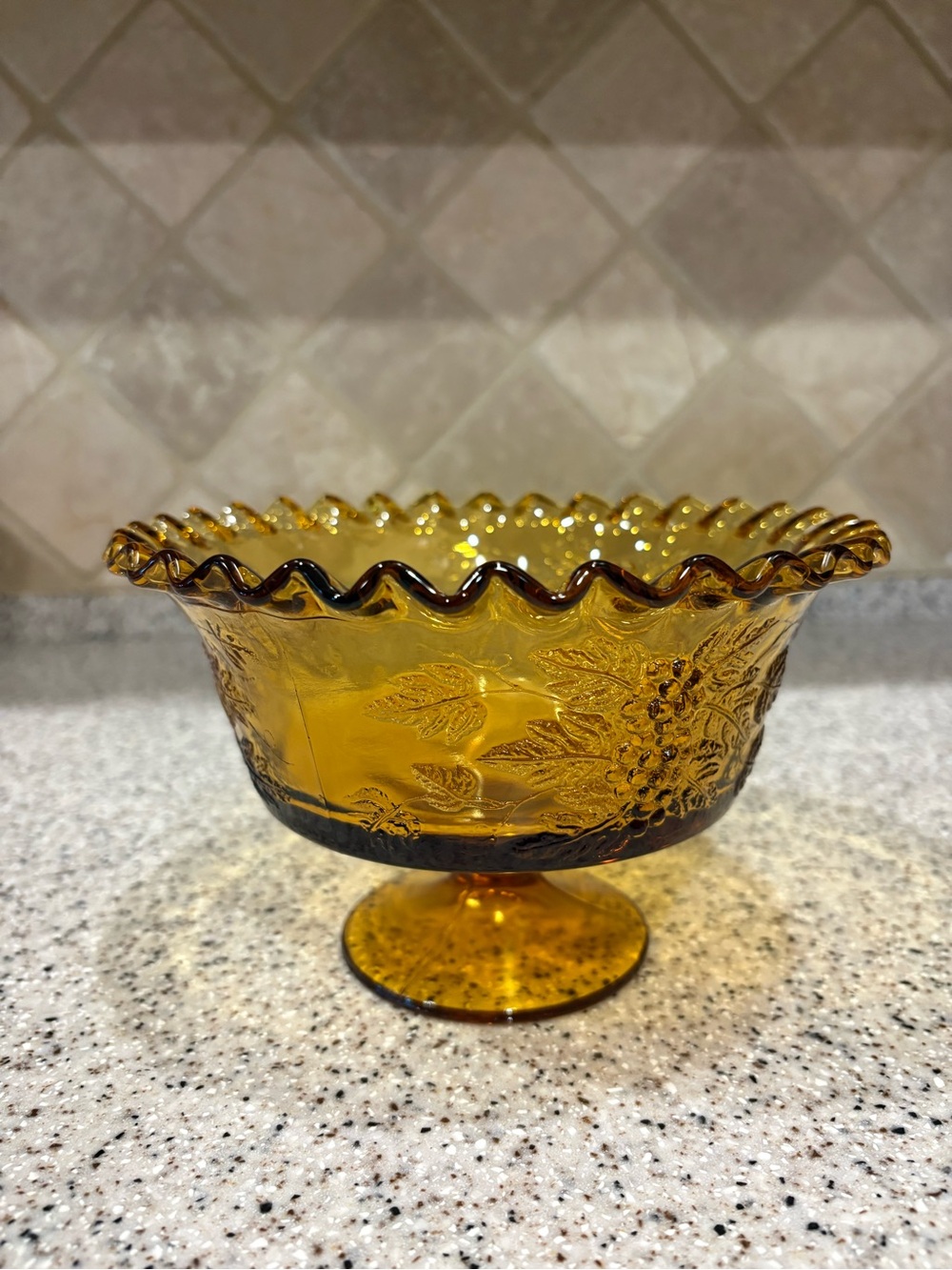 Vintage amber glass pedestal compote featuring a classic embossed grape and leaf